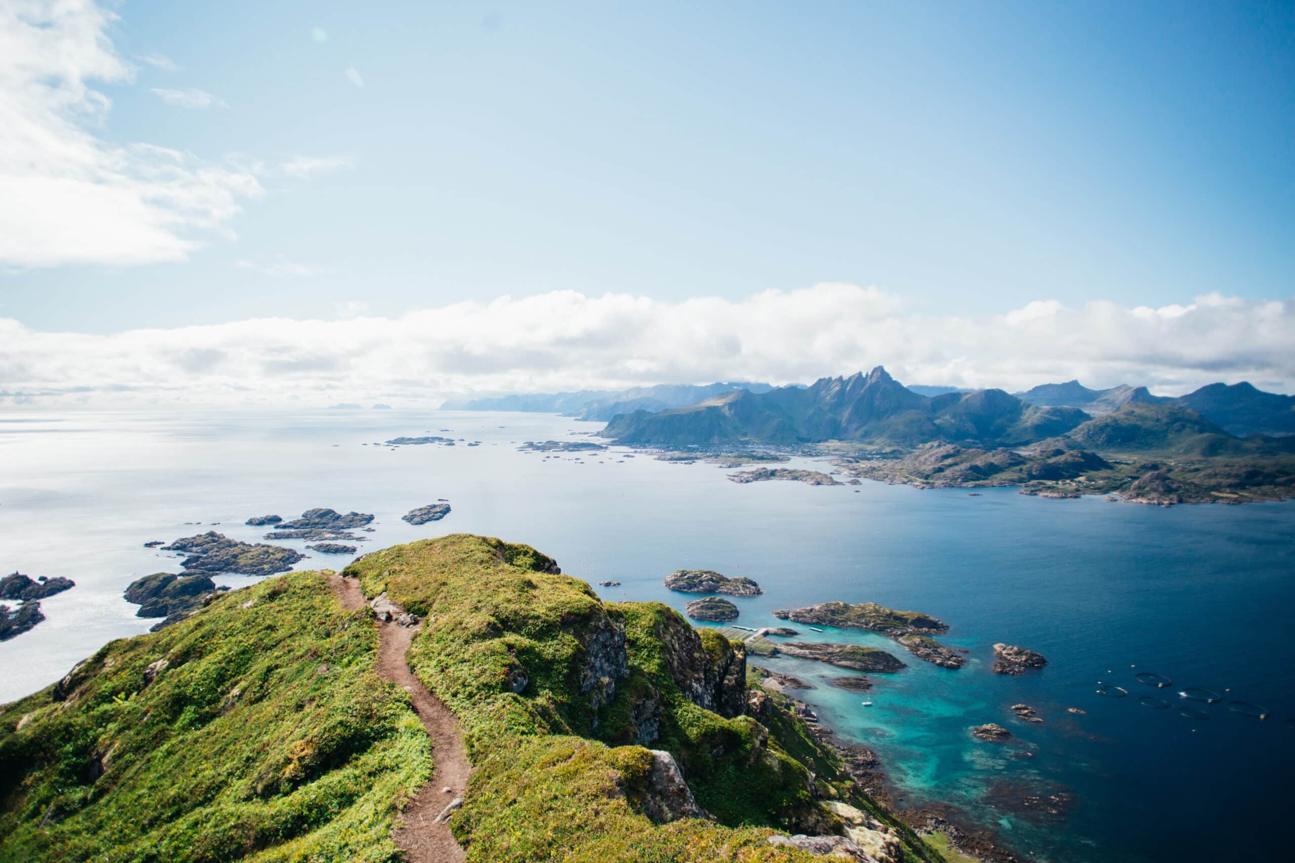 Amazing epic shot of young man hiker stand on top of mountain after long difficult hike in Lofoten Islands in Norway. Incredible summer views of scandinavian travel lifestyle. Epic landscape in north